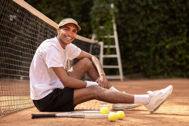 After workout. Man in white tshirt and sun visor resting at the tennis courts - Photo, Image