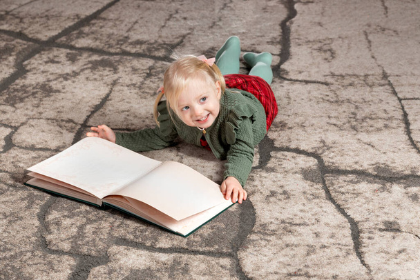 Two-year-old girl lies on floor and flips through book with blank empty pages. Copy space. Christmas eve. - Photo, Image