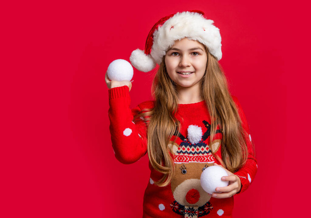 teen girl in santa hat with snowball on red new year background with copy space. new year teen girl in santa hat hold snowball. teen girl wear sweater hold new year snowball. happy new year. - Photo, Image