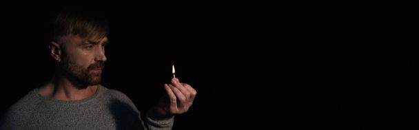 homem segurando fósforo iluminado durante queda de energia isolado em preto, banner - Foto, Imagem