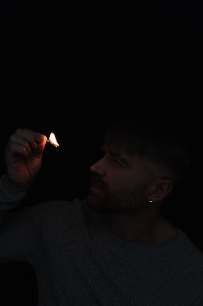homem olhando para chama de queima de fósforo durante queda de energia isolado em preto - Foto, Imagem