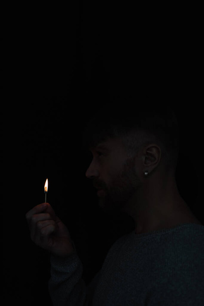 vista lateral del hombre sosteniendo fuego partido durante el apagón de energía aislado en negro - Foto, Imagen