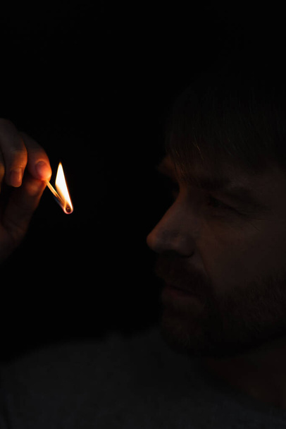 man looking at flame of burning match in darkness isolated on black - Foto, Imagem