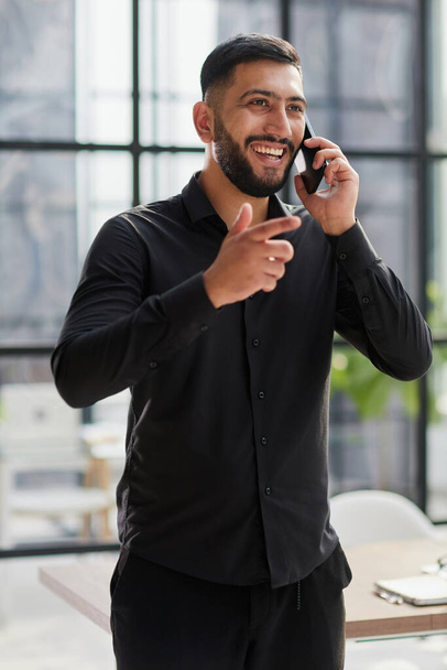 young man in a black shirt talking on the phone in the office - Fotoğraf, Görsel