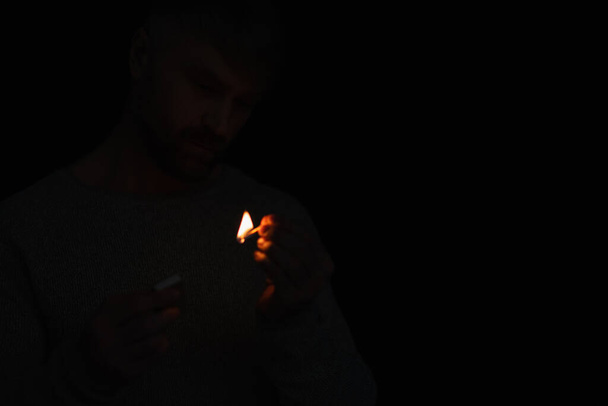 Mann mit Streichholzschachtel sieht brennendes Streichholz bei Stromausfall isoliert auf schwarz - Foto, Bild