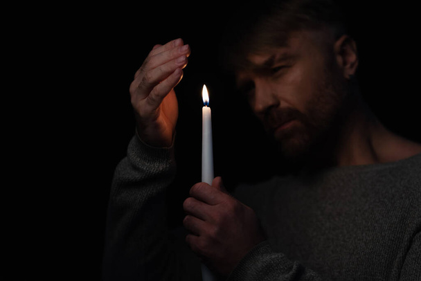 hombre en la oscuridad causada por el apagón de energía sosteniendo vela encendida aislada en negro - Foto, imagen