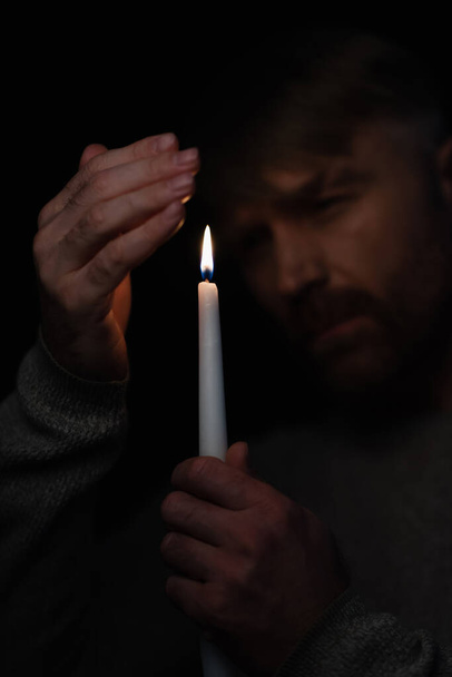 mężczyzna trzymając się za rękę przy świecy i patrząc na płonący płomień izolowany na czarno - Zdjęcie, obraz