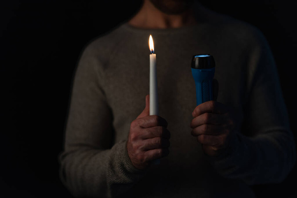 partial view of blurred man with burning candle and flashlight isolated on black - Foto, immagini