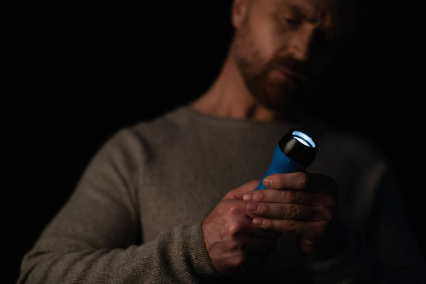 blurred man holding glowing flashlight during energy blackout isolated on black - Foto, Imagen