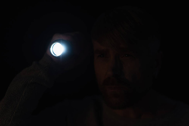 Mann mit heller Taschenlampe schaut in der Dunkelheit isoliert auf schwarz weg - Foto, Bild