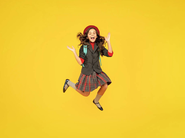 glad teen girl in uniform and beret with school bag running on yellow background, schoolgirl. - Zdjęcie, obraz