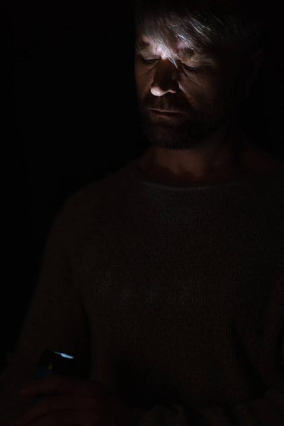 Mann mit glühender Taschenlampe beleuchtet sein Gesicht während Stromausfall isoliert auf schwarz - Foto, Bild