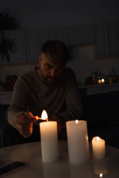 hombre sentado en la cocina oscura durante el corte de energía y la iluminación de velas - Foto, Imagen