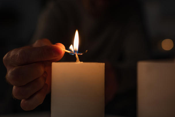 cropped view of man with burning match lighting candle on black background - Fotó, kép