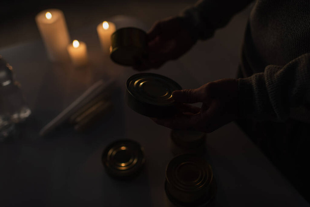 partial view of man with canned food near candles burning during power outage - Photo, Image
