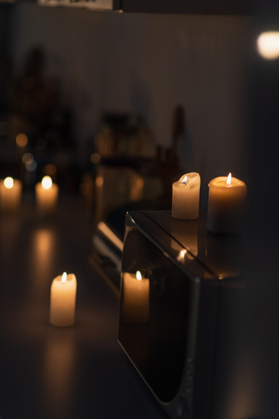горящие свечи на микроволновой печи и кухонном столе в темноте, вызванной отключением электричества - Фото, изображение