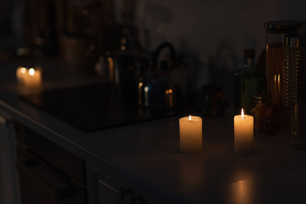 Enerji kesintisi sırasında mutfak tezgahında mutfak gereçleri ve yanan mumlar. - Fotoğraf, Görsel