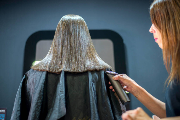 Close-up of a hairdresser hand cutting the ends of her blonde hair with an electric razor. Beauty salon. Professional hair care. - Photo, Image