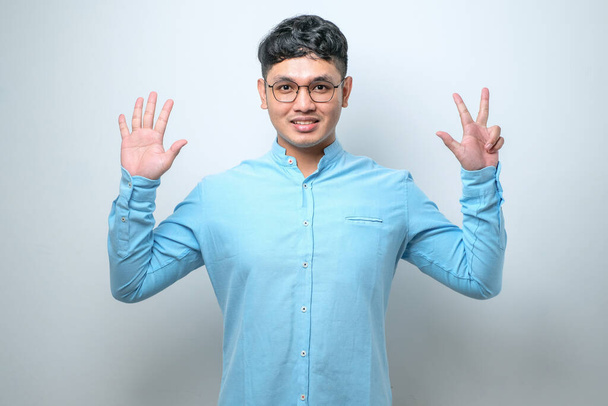 Mladý asijský muž na sobě ležérní oblečení ukazující a ukazující nahoru s prsty číslo osm při úsměvu sebevědomě a šťastně přes bílé pozadí - Fotografie, Obrázek
