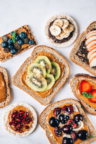 Various kind of open sandwiches with berries and fruits. Made from bread, such as wholegrain, rice crakers, crispbreads and different nut butter, such as peanut, crunchy cashew and almond butter - Fotoğraf, Görsel