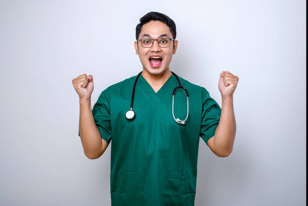 Захоплений азіатський лікар, який носить скраби та окуляри, робить виграшні конгреси жестів або хвалить когось ізольованого на білому тлі
 - Фото, зображення