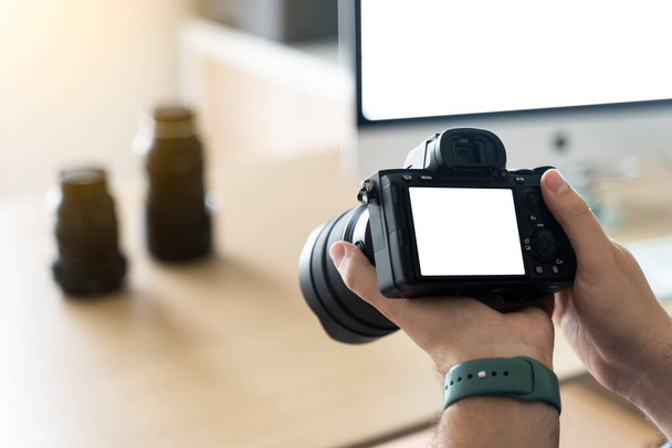 Nahaufnahme einer Fotokamera mit Tisch, Computer und Objektiven im Hintergrund - Foto, Bild