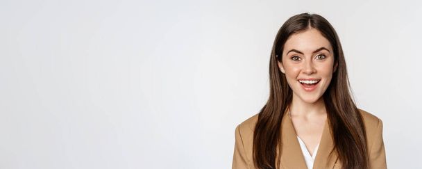 Close up portrait of enthusiastic corporate woman, looking amazed and excited at camera, standing in suit over white background. - Photo, Image