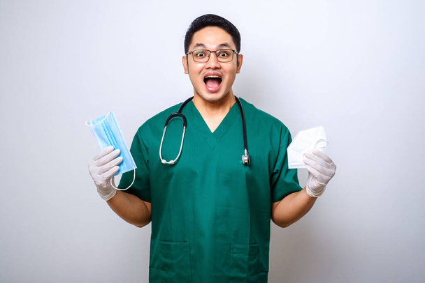 Alegre joven asiático médico masculino, enfermera en matorrales, sonriendo y la entrega de máscaras médicas para la seguridad del paciente aislado sobre fondo blanco - Foto, Imagen