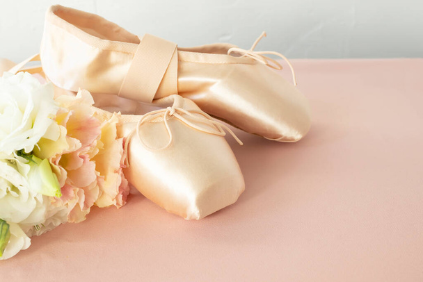 Pink ballet pointe shoes and a bouquet of delicate fresh flowers on a pink background. - Photo, image