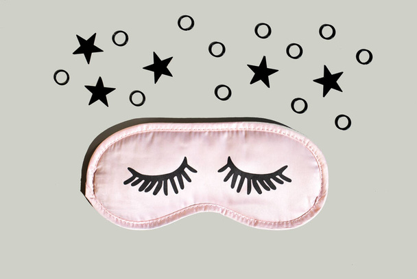 Máscara de sono rosa com pestanas em um fundo cinza com estrelas pretas. Conceito de sono saudável. Espaço para texto, vista superior. - Foto, Imagem