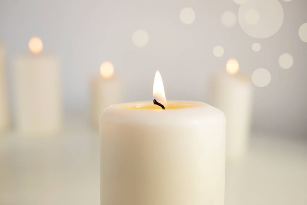 Ένα μεγάλο λευκό κερί ανάβει σε λευκό φόντο. - Φωτογραφία, εικόνα
