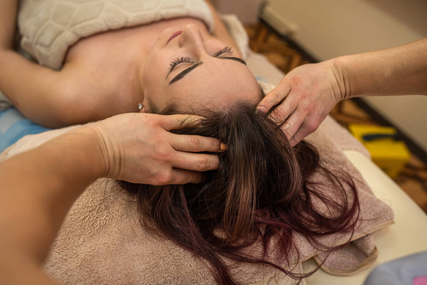 the best masseuse with gentle hands massages the head and face for the best client with a beautiful face. Relaxing massage concept - Valokuva, kuva
