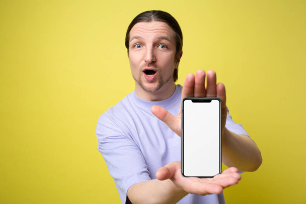 Захоплений чоловік тримає великий смартфон з білим порожнім екраном в руці, показуючи близько до камери на жовтому тлі. Гаджет з порожнім вільним місцем для сміху, банер
 - Фото, зображення