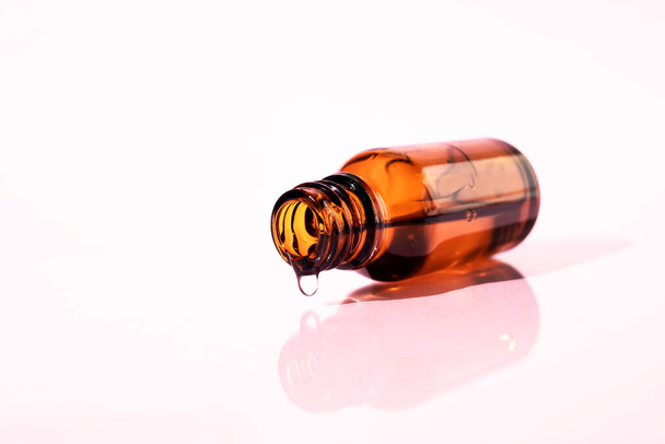 A glass bottle with a gel-like liquid inside on a pink background. Side view, place for text. - Photo, Image
