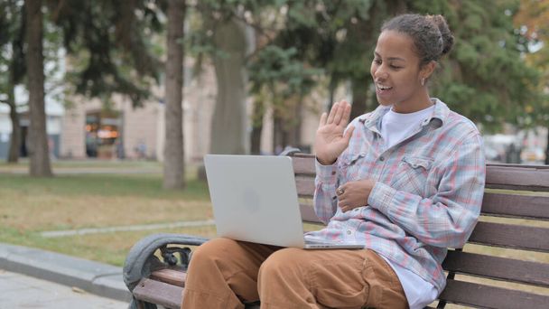 Young African Woman Talking on Video Call while Sitting Outdoor on Bench - Foto, afbeelding