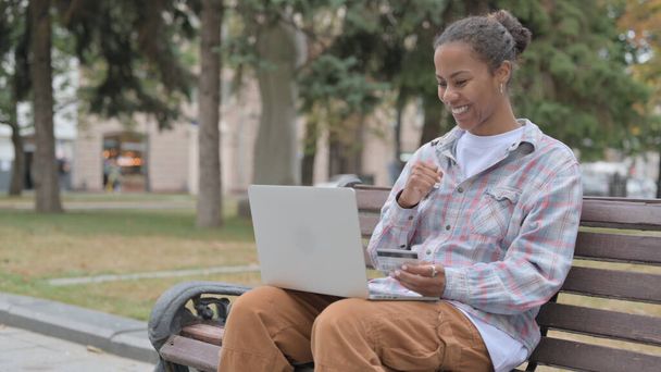 Online Shopping by Excited Young African Woman while Sitting Outdoor on Bench - Foto, imagen