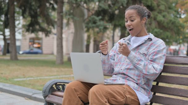 Young African Woman Celebrating Success on Laptop while Sitting Outdoor on Bench - Fotografie, Obrázek