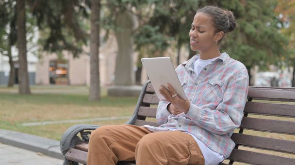 Молода африканка реагує на втрату планшета сидячи на відкритому повітрі на лавці
 - Фото, зображення