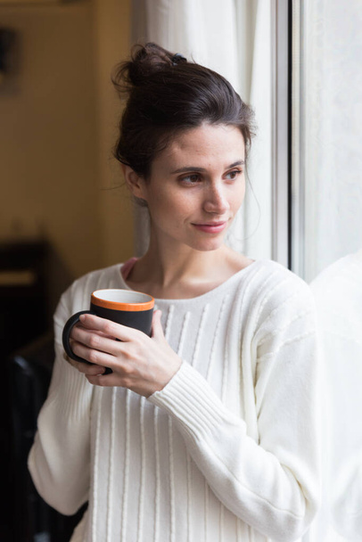 Woman alone at home having a hot beverage looking out of a window. - Photo, Image