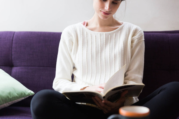 Woman sitting indoors on a sofa reading a book alone. - Fotografie, Obrázek