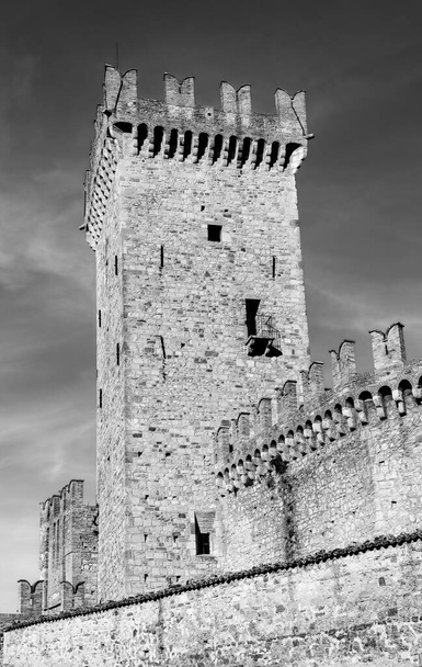 Torre in pietra di un castello medievale con una piccola sezione del muro contro il cielo con nuvole. Foto in bianco e nero - Foto, immagini