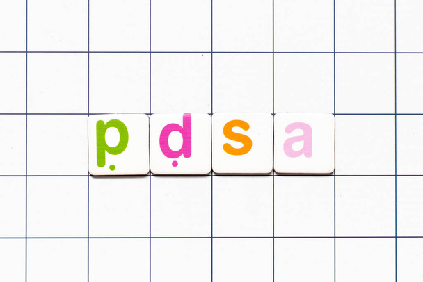 Carta azulejo colorido en la palabra PDSA (Abreviatura del plan de hacer acto de estudio) sobre fondo de rejilla blanca - Foto, Imagen