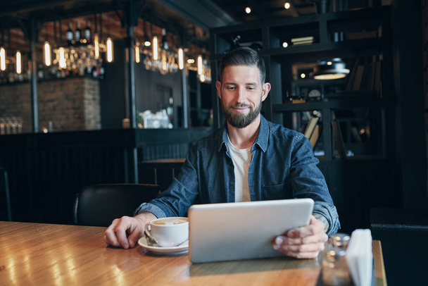 Jeune homme buvant du café dans un café et utilisant une tablette. Indépendante. En milieu de travail. Déjeuner
 - Photo, image