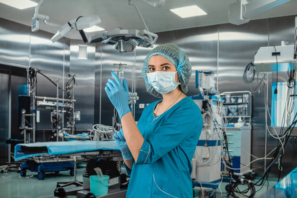 Retrato de uma bela médica cirurgiã usando luvas médicas em pé na sala de cirurgia. Um cirurgião numa sala de operações moderna. medicina. sala de cirurgia - Foto, Imagem
