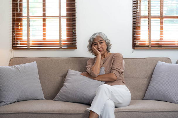 Nachdenkliche reife Frau, die allein zu Hause auf dem Sofa sitzt, träumt und plant, ernsthaft nachdenkliche ältere Seniorin, die in die Ferne schaut, im Wohnzimmerfenster. - Foto, Bild