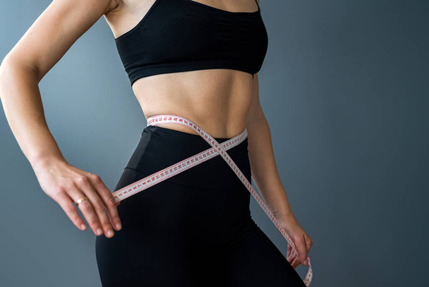 Sporty ταιριάζει γυναίκα μέτρησης με μεζούρα και τη μέτρηση της μέσης μετά από δίαιτα απομονώνονται σε γκρι φόντο. Διαιτολογία. Γυμναστική απώλεια βάρους. μέτρηση μεγέθους - Φωτογραφία, εικόνα