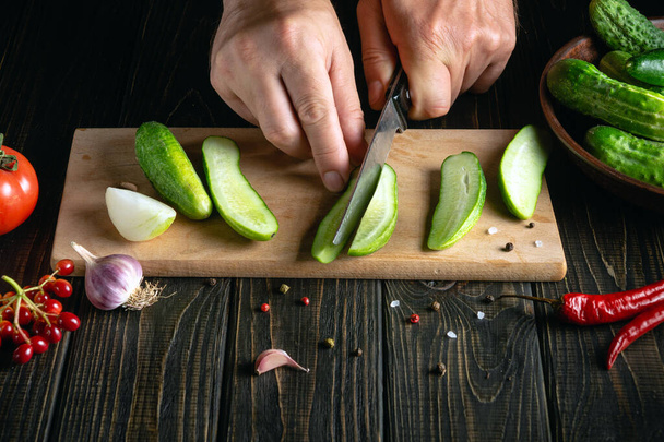 Chef corta pepinos frescos para decapar con especias y verduras. Primer plano de las manos de un cocinero mientras trabaja en la mesa de la cocina en un restaurante - Foto, Imagen