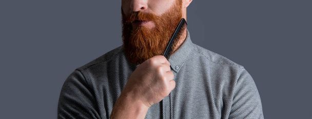 cropped view of man has beard in studio. man combing beard with haircomb. combing and styling. bearded man combing beard isolated on grey background. man with beard combing hair. - Photo, image