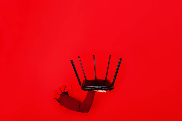 router wifi negro en la mano sobre fondo rojo, imagen de diseño - Foto, Imagen