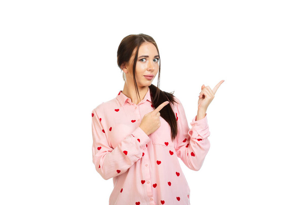 Молодой, красивый спокойный девушка изолированы на белом фоне в розовой рубашке с красными сердцами, указывает пальцами на место для продвижения по службе, предложения или рекламы. - Фото, изображение
